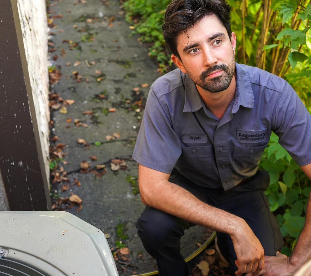 HVAC technician kneeling outdoors beside equipment